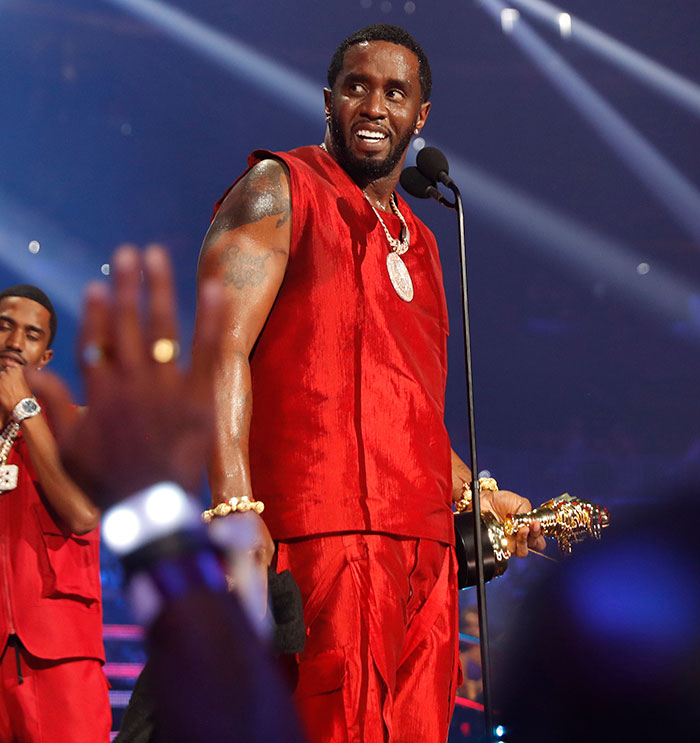 Diddy on stage in red outfit holding a trophy as Diddy's trial turns chaotic with surprise jury note after deliberations.