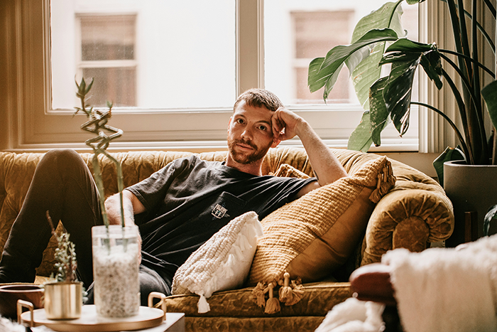 Man looking stumped while sitting on a couch, reflecting on generational trauma and family apology demands. - 7