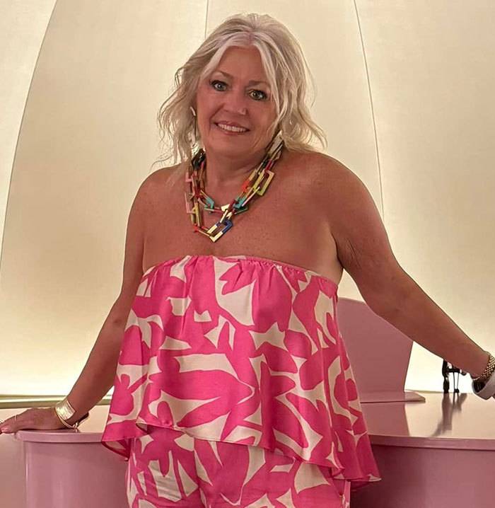 Woman in a pink patterned dress and colorful necklace posing indoors, related to girl's fall from Disney cruise ship incident.