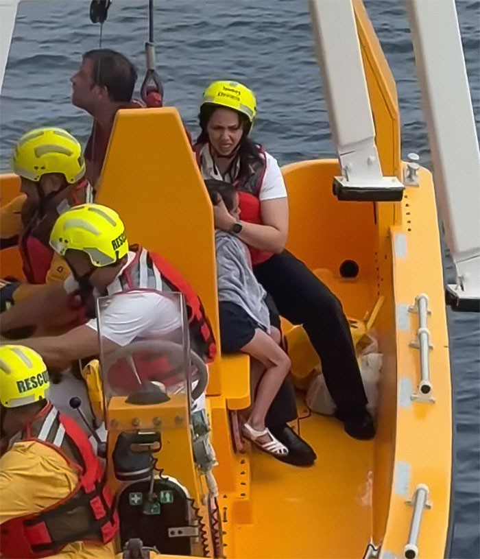 Rescue team wearing helmets and life vests comforting a girl during Disney cruise ship fall incident on a rescue boat.