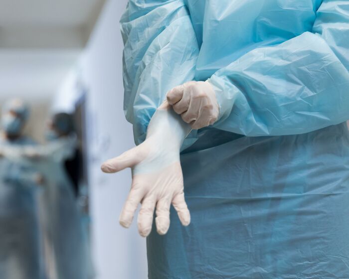 Person in blue protective gown putting on gloves, illustrating people who deal with dead bodies in a clinical setting.