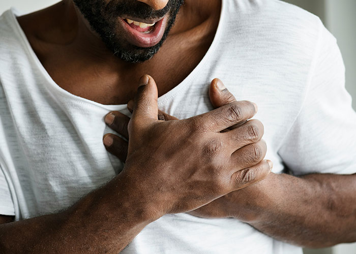 Man clutching chest in pain, illustrating patients delaying help with shocking health consequences and symptoms. - 20
