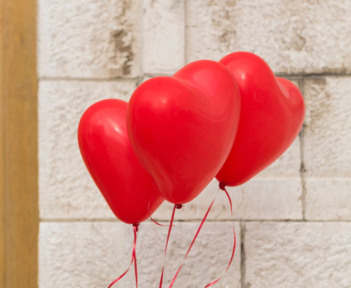 Three red heart-shaped balloons floating indoors, symbolizing a man’s romantic plans and love theme. Three red heart-shaped balloons floating indoors, symbolizing a man’s romantic plans and love theme.