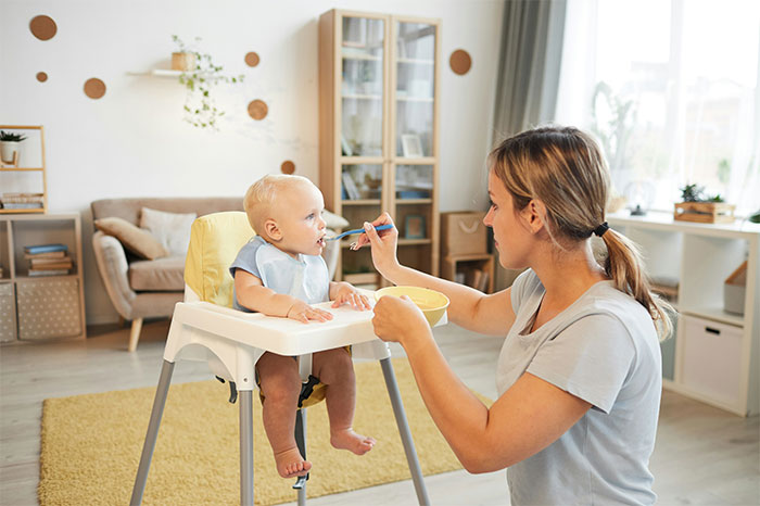 Mother feeding baby in high chair at home, capturing a moment of realizing something was done the wrong way. - 6