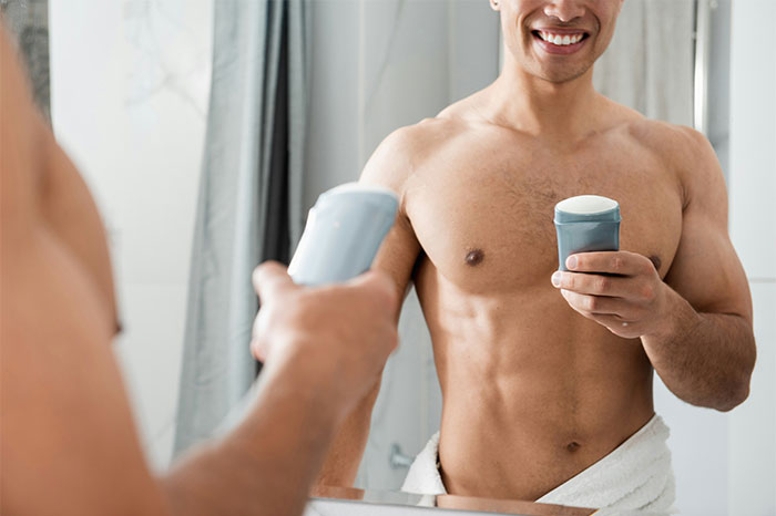 Man with towel around waist applying deodorant in front of mirror, illustrating people doing things the wrong way moments. - 12