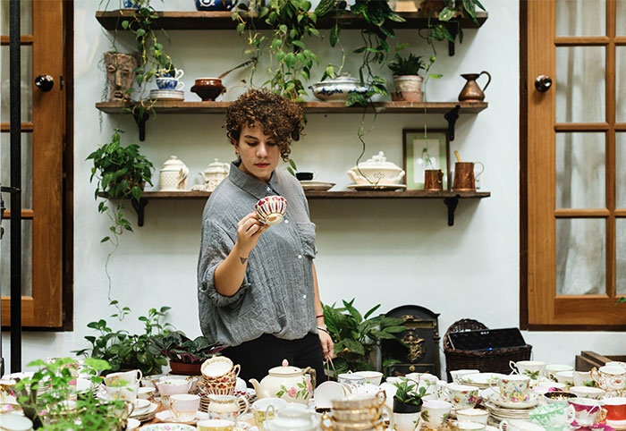 Woman with curly hair surrounded by teacups and plants, realizing she was doing something the wrong way in a cozy room. - 32