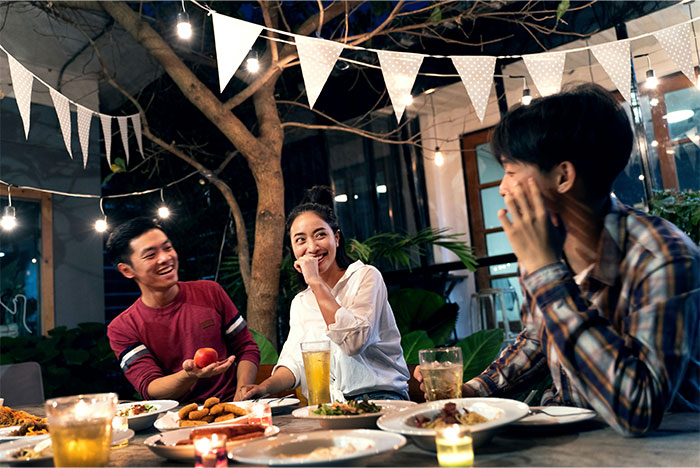 Three friends laughing and sharing moments at a decorated outdoor dinner party under string lights and banners. - 19