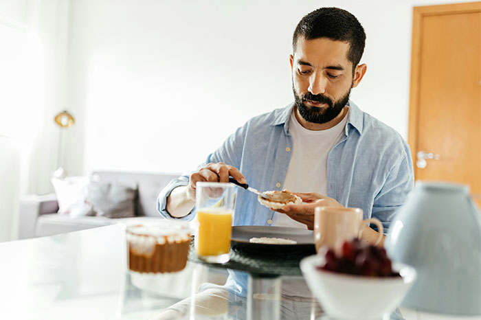 Man spreading peanut butter on bread at breakfast, capturing a not my proudest moment realization about doing something wrong. - 18