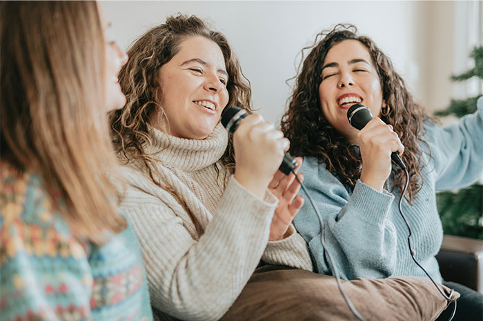 Three friends happily singing karaoke indoors, enjoying a fun moment despite doing it the wrong way. - 22