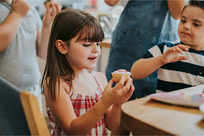 Young girl holding a cupcake at a table, surrounded by children, capturing a moment of realizing the wrong way. - 35