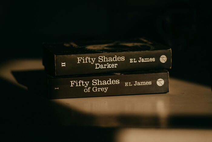 Two Fifty Shades books by EL James stacked on a table, symbolizing red flags often romanticized in relationships. - 9