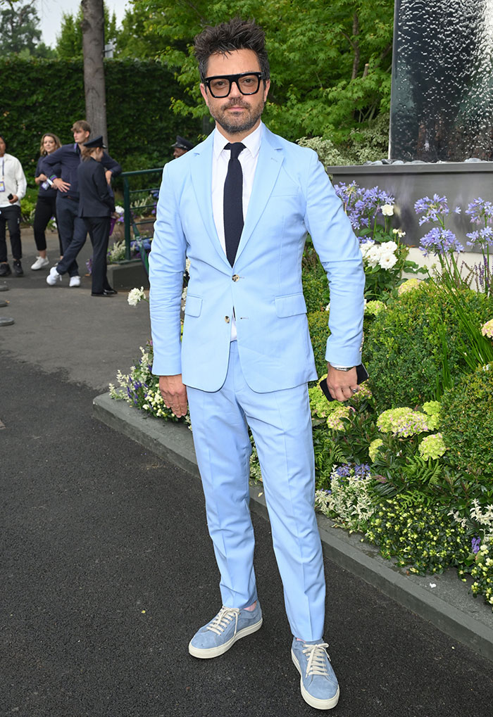 Man in light blue suit and sneakers posing at Wimbledon 2025 among celebrity looks and garden flowers.