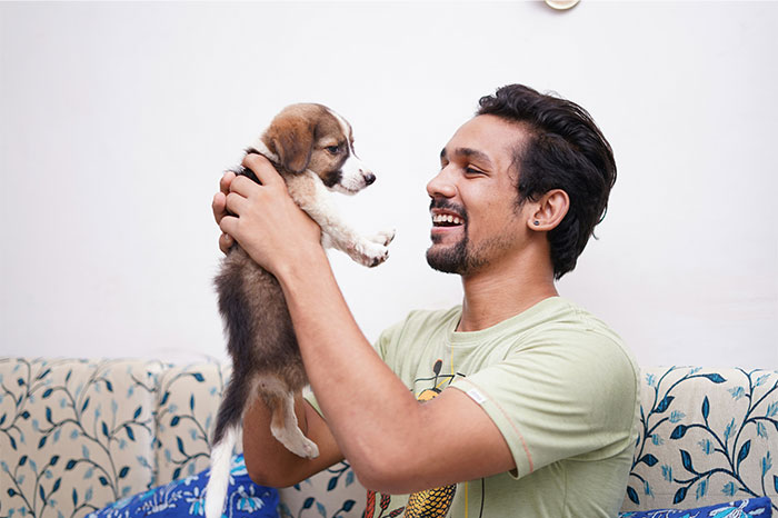 Man holding a puppy indoors, smiling and engaging in a moment of kindness and connection with the pet. - 2