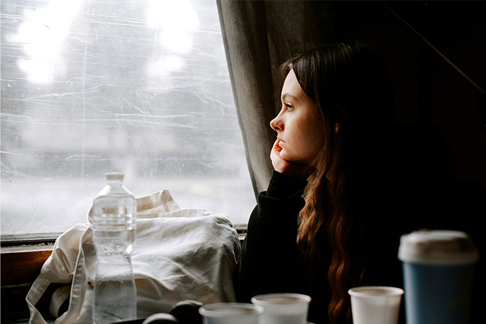 Young woman looking pensively out a window, reflecting moments when people decided to stop helping others out. - 12