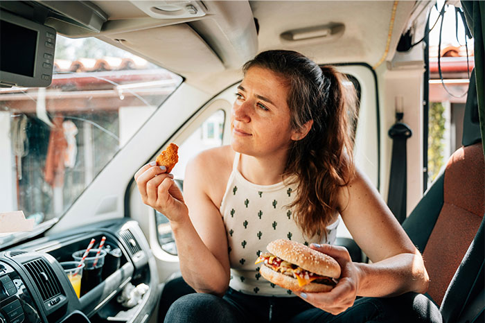 Woman inside a vehicle holding a burger and nugget, illustrating moments people decided to stop helping others out. - 27