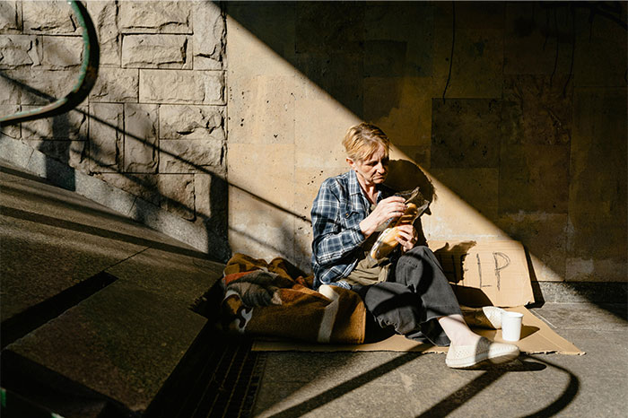 Person sitting alone in a shaded corner with a cardboard sign, illustrating moments people decided to stop helping others. - 28