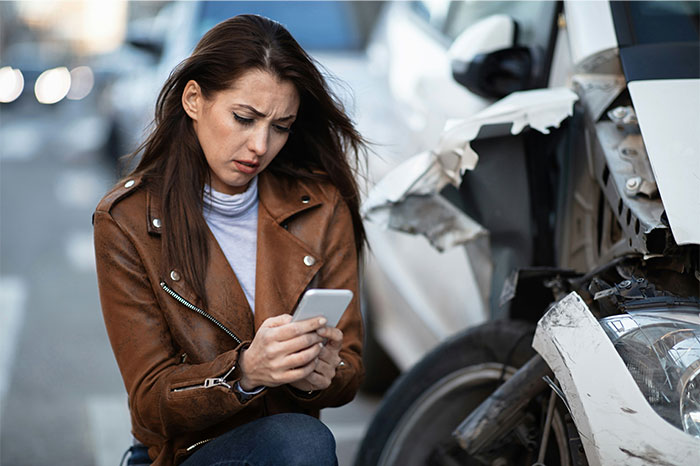 Woman looking upset while using phone near a damaged car, illustrating moments people decided to stop helping others out. - 9