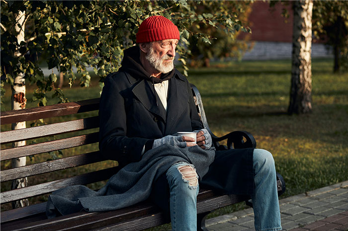 Elderly man in a red hat sitting alone on a park bench, reflecting on times people decided to stop helping others. - 32