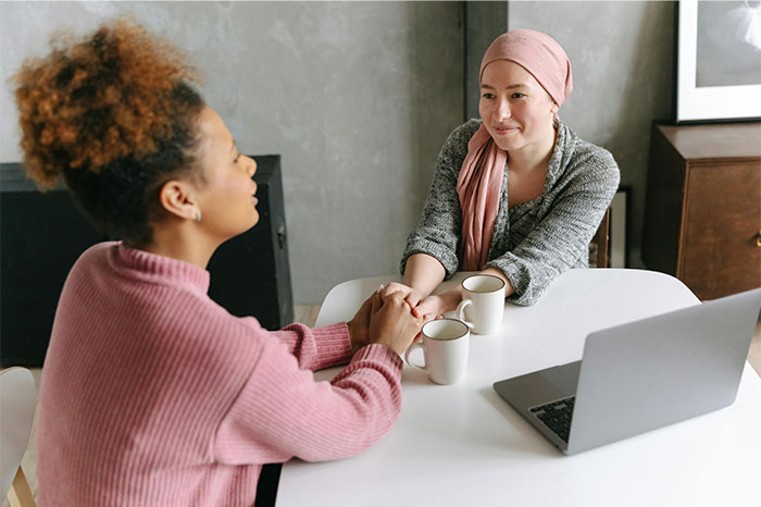 Two women holding hands across a table with coffee cups and laptop, showing a moment of support and connection. - 6