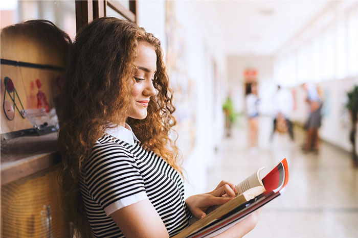 Young woman with curly hair reading a book in a hallway, reflecting on times people decided to stop helping others out - 3