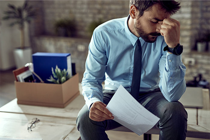 Man in office attire sitting stressed and holding papers, depicting frustration after deciding to stop helping others out. - 23