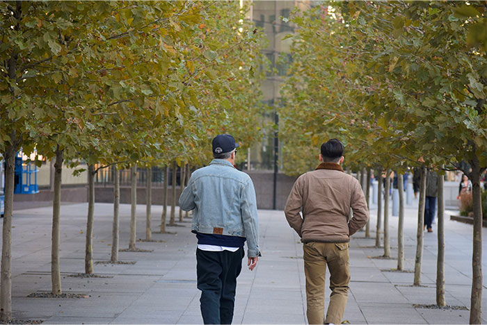 Two men walking away on an urban sidewalk lined with trees, illustrating moments of people deciding to stop helping others. - 34