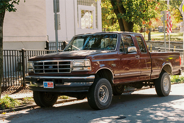 Brown Ford F150 pickup truck parked on a street with shadows and a fence in the background. - 14