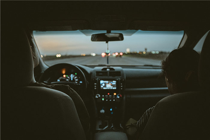 View from inside a car at night with two people sitting in the front seats on a dark road ahead. - 37