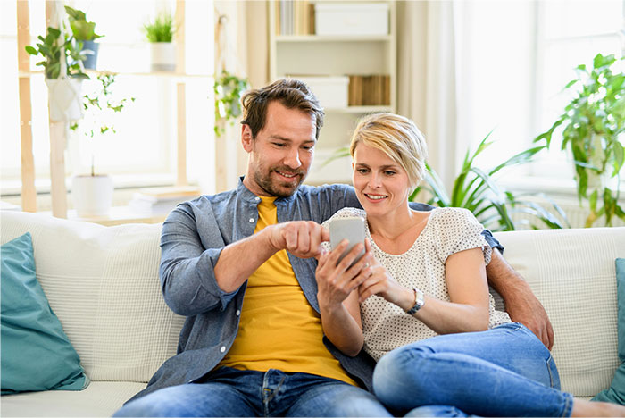 Couple sitting on a couch together, smiling and looking at a smartphone, capturing moments of stopping helping others behavior. - 24