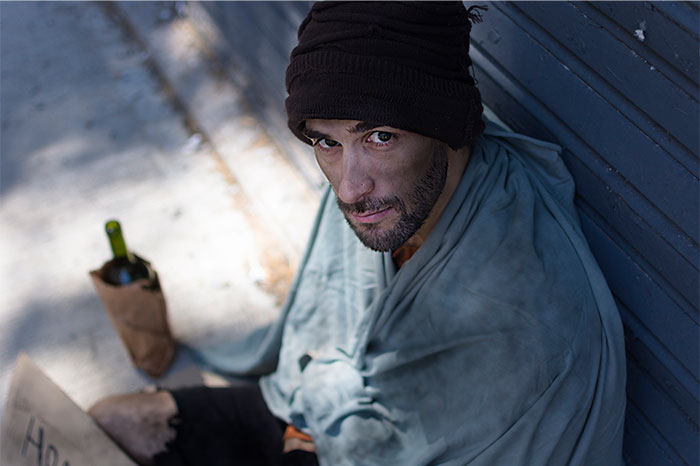 A man in a beanie and blanket sitting on the street, representing times people decided to stop helping others. - 42