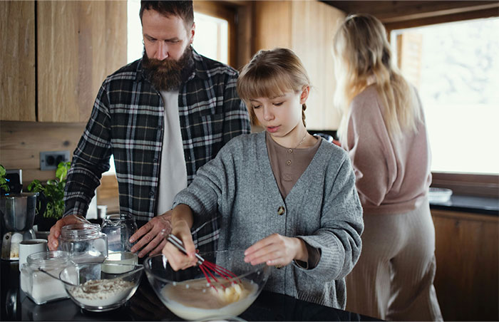 A family in a kitchen with a child mixing ingredients while an adult watches, reflecting moments people decided to stop helping others. - 48