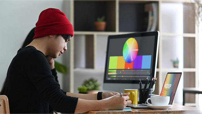 Young man wearing a red beanie working on color grading at a computer, symbolizing times people stopped helping others out. - 25
