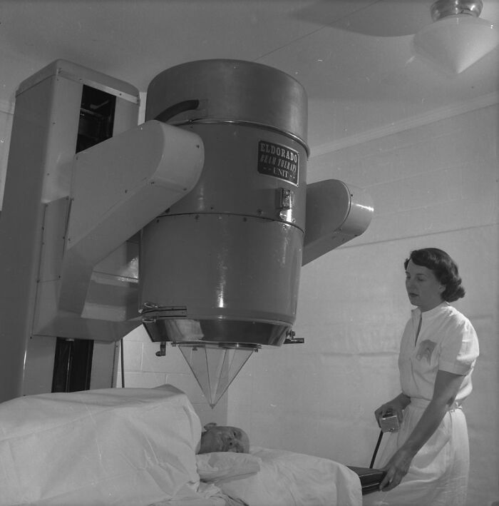 Large unsettling medical device from the past with a nurse attending to a patient lying in bed in a vintage clinical setting.