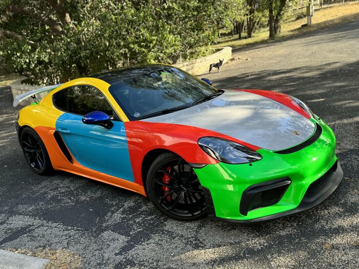 Colorfully painted sports car with unique outrageous car mods parked on a driveway surrounded by trees.