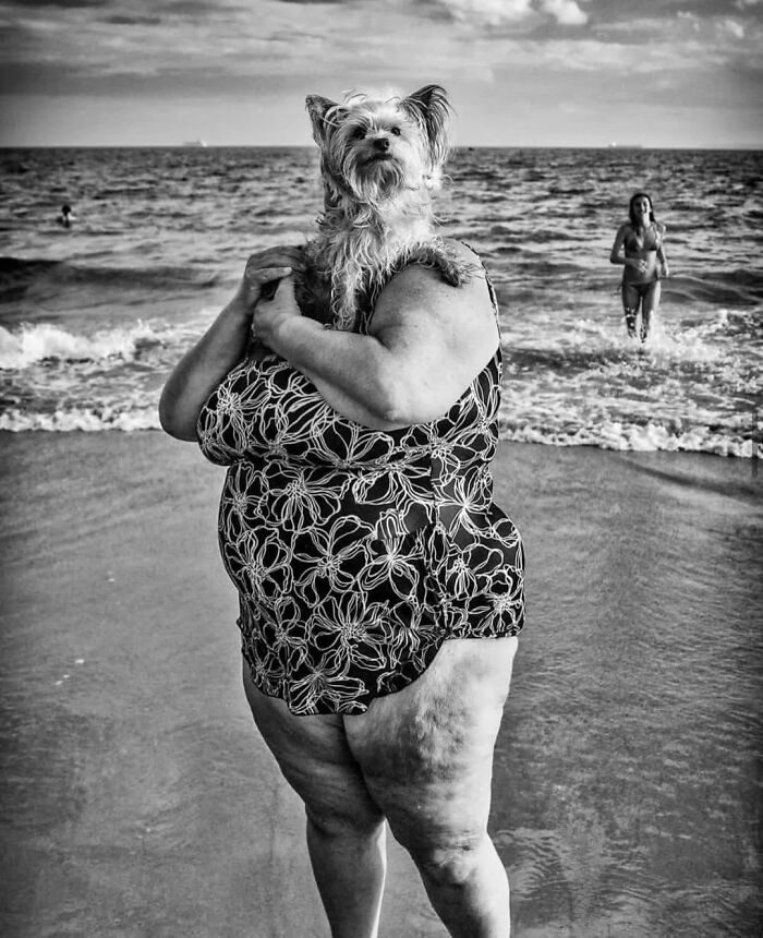 Person at the beach holding a small dog on their shoulder, a random animal sighting captured perfectly on the street.