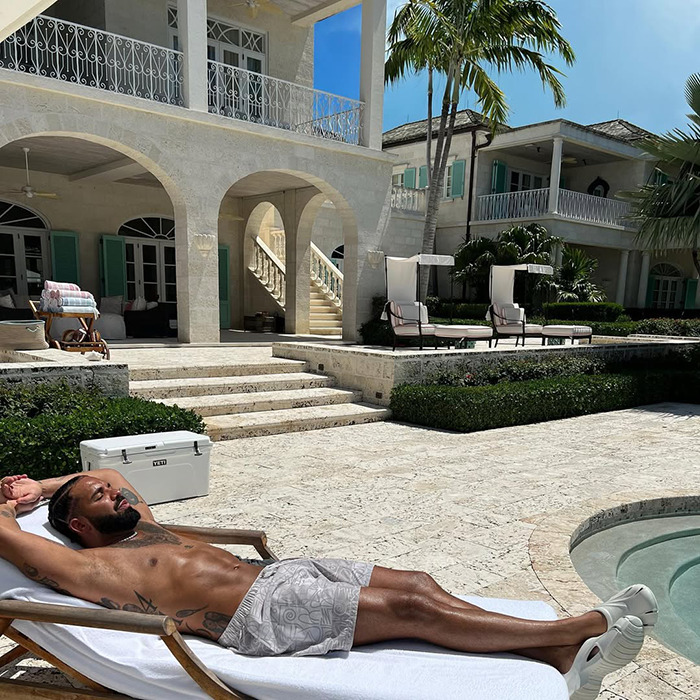 Man with shirtless abs lounging by pool at luxury villa, raising questions about plastic surgery for six-pack appearance.
