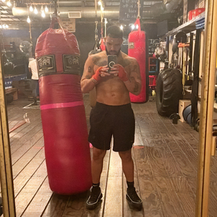Drake shirtless selfie in gym with red punching bag, showing abs questioned for possible plastic surgery.
