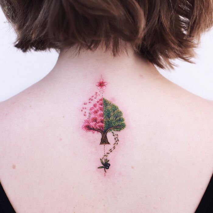 Intricate tattoo of a half blossom and half green tree with butterfly details on the upper back, unique tattoo design.