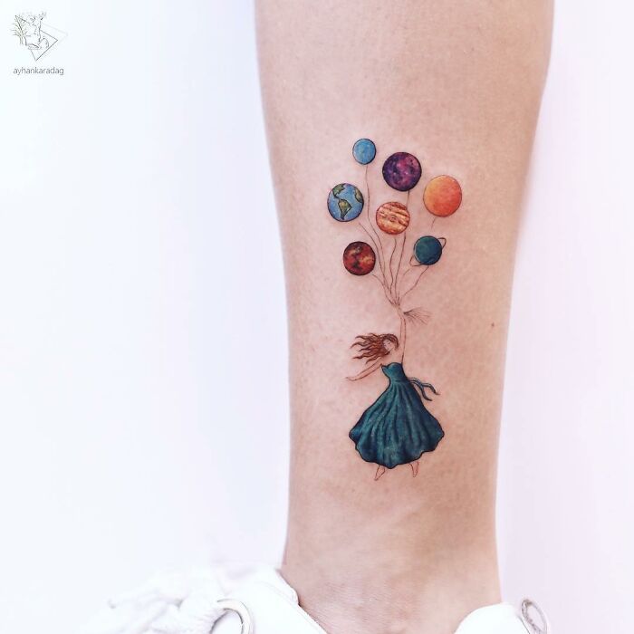 Colorful tattoo of a woman in a dress holding planet balloons on a lower leg, showcasing one of the best tattoos.