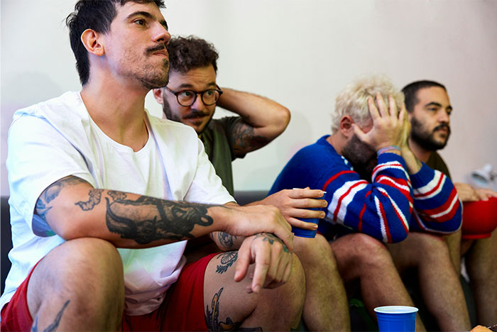 Group of men sitting closely, appearing concerned and thoughtful, reflecting on a tense situation with a drunk wife and violence. - 7
