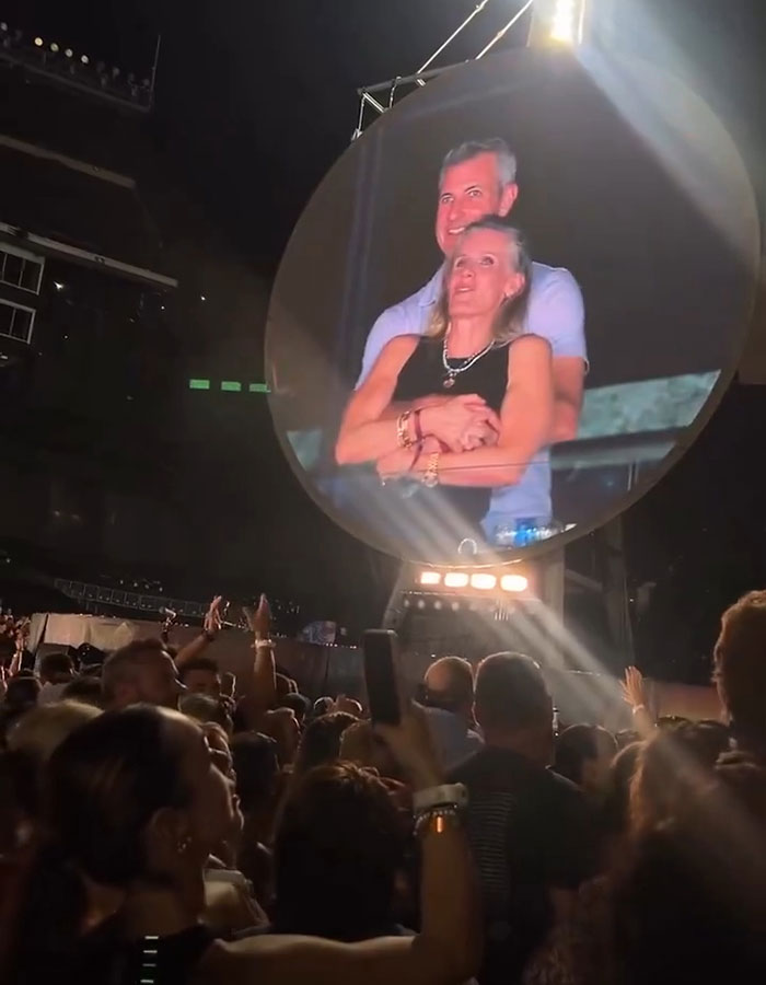 Couple featured on kiss cam screen at Coldplay concert with crowd watching during live music event.