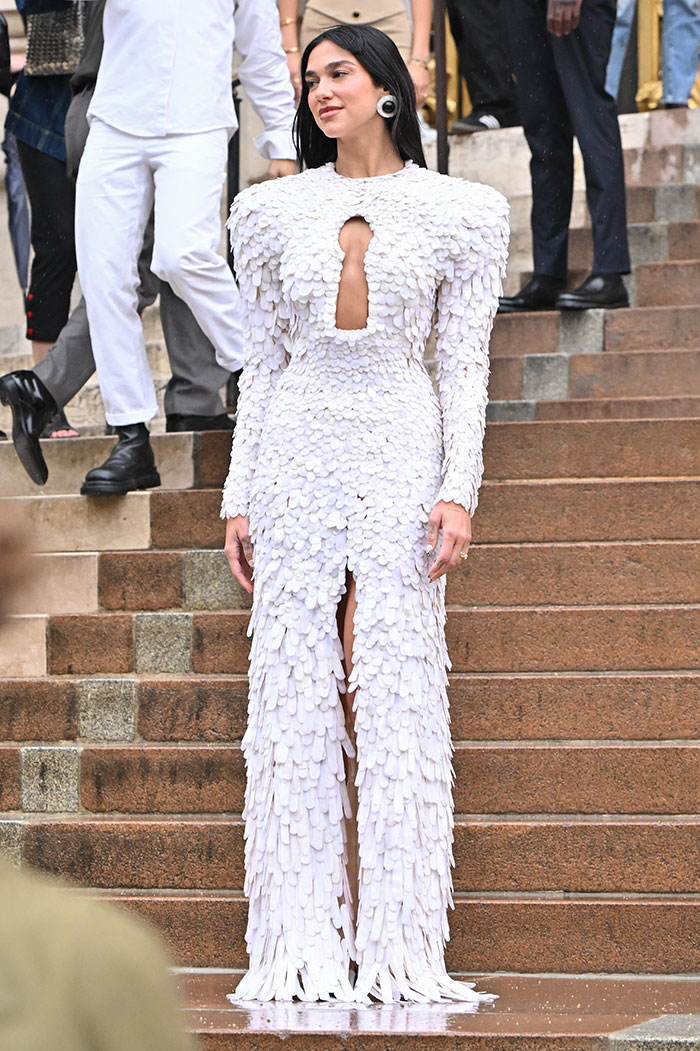 Celebrity wearing a textured white gown with shoulder pads and a front slit, attending Paris Fashion Week 2025 viral looks. Celebrity wearing a textured white gown with shoulder pads and a front slit, attending Paris Fashion Week 2025 viral looks.