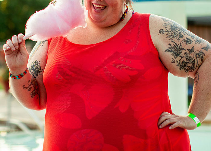 Smiling person in red dress holding cotton candy, showing tattoos on arms in outdoor setting, highlighting dumbest reasons risks.
