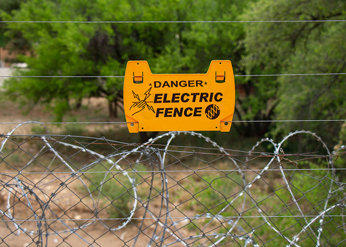 Yellow danger electric fence warning sign on barbed wire fence in outdoor green area showing risks that almost cost lives