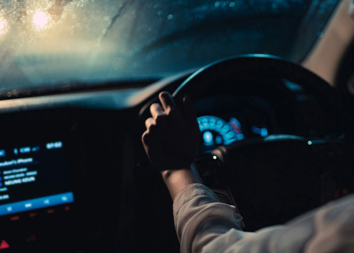 Driver gripping steering wheel tightly at night inside car, illustrating dumbest reasons that almost cost lives.