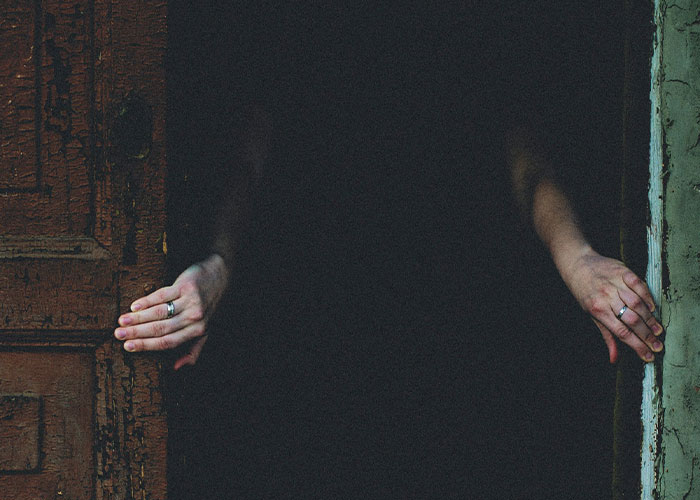 Person cautiously opening a dark door with both hands, illustrating one of the dumbest reasons that almost cost lives.