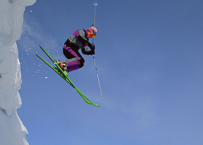 Skier in colorful outfit jumping off snowy cliff, illustrating dumbest reasons that almost cost people their lives.