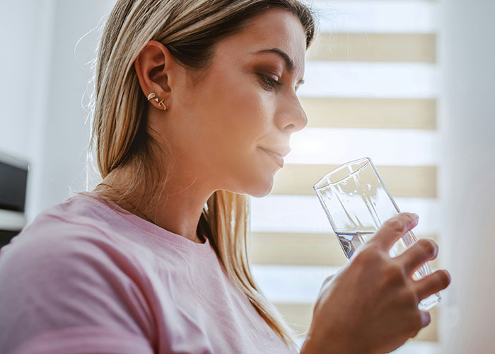 Young woman drinking water indoors, illustrating one of the dumbest reasons that almost cost people their lives.