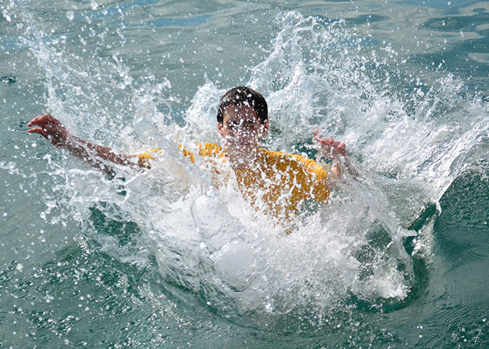 Boy wearing yellow shirt falling into water creating a large splash, illustrating dumbest reasons that almost cost lives.