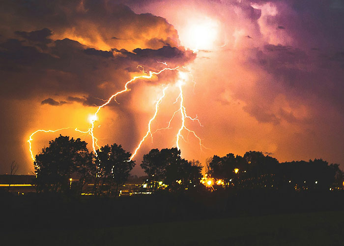 Lightning striking behind trees during a stormy night, illustrating dumbest reasons that almost cost people their lives risks.